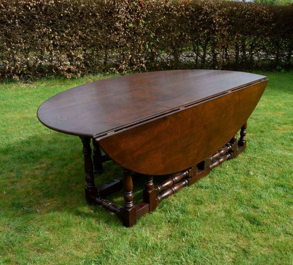An early twentieth-century dark oak oval wake dining table with two drop-leaf flaps, turned legs, and base stretchers. View VIII