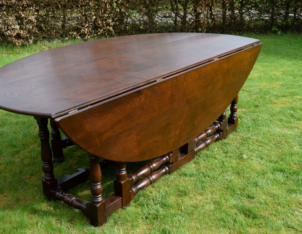 An early twentieth-century dark oak oval wake dining table with two drop-leaf flaps, turned legs, and base stretchers. View IX