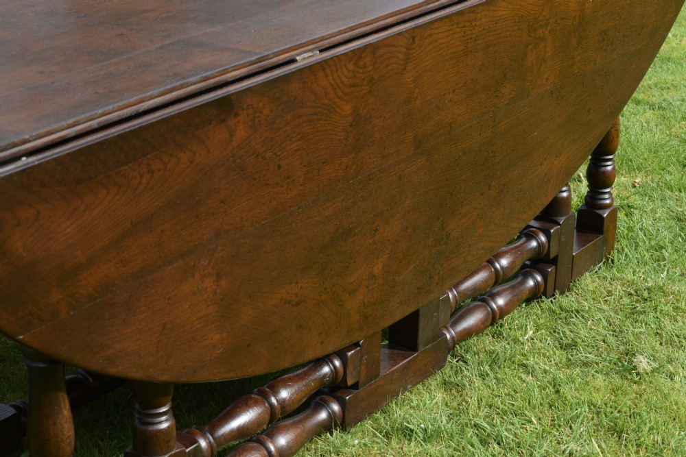 An early twentieth-century dark oak oval wake dining table with two drop-leaf flaps, turned legs, and base stretchers. View X