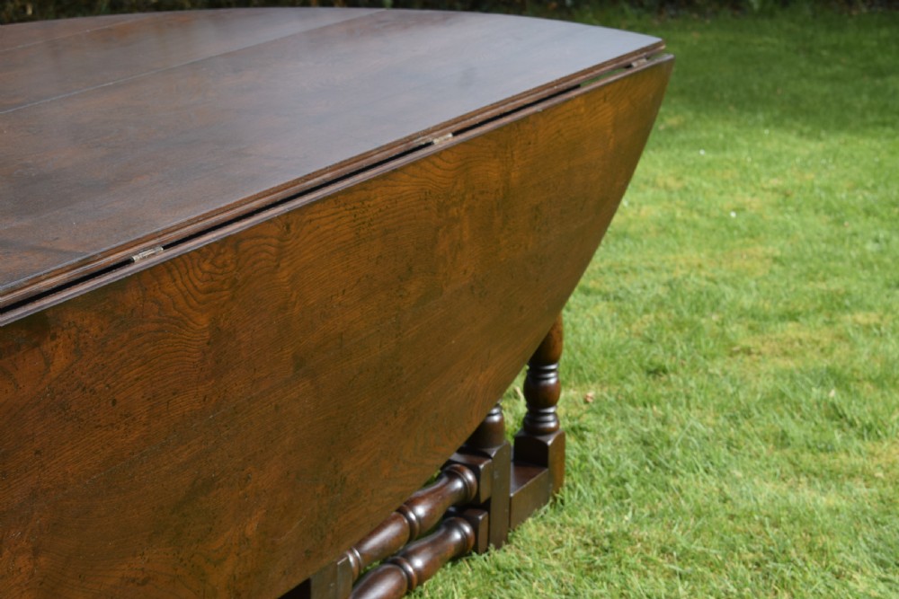 An early twentieth-century dark oak oval wake dining table with two drop-leaf flaps, turned legs, and base stretchers. View XI