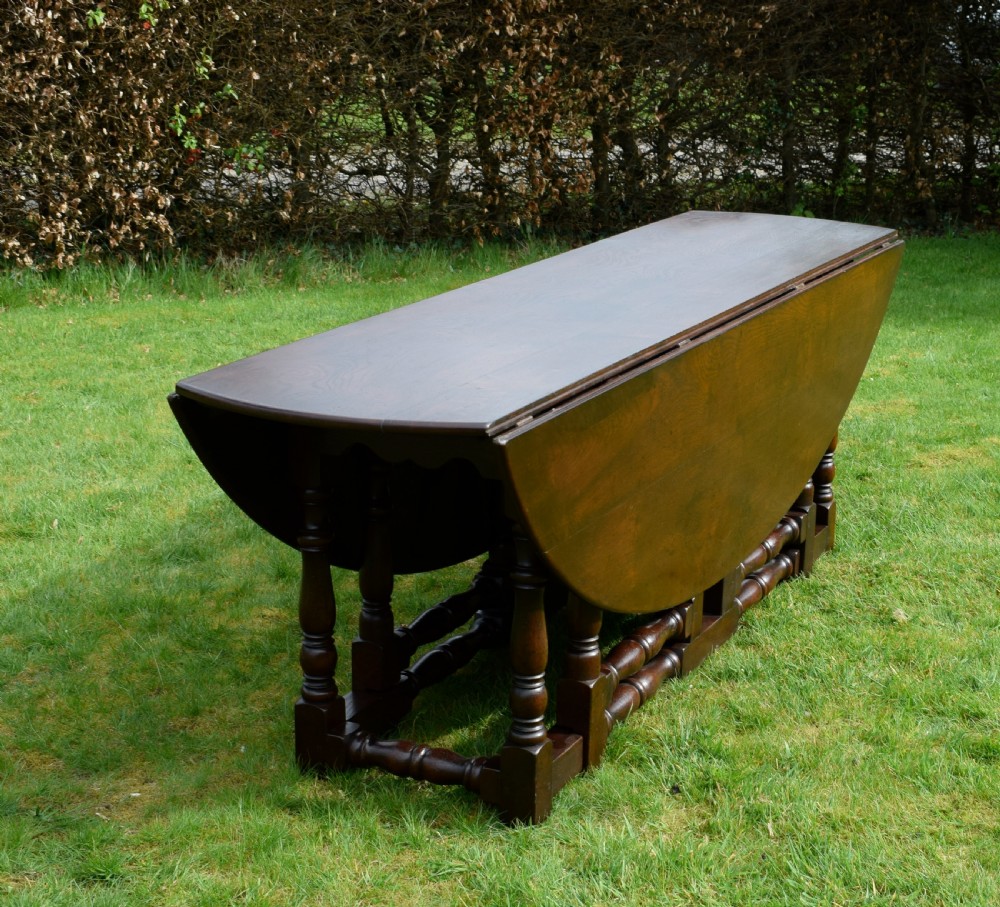 An early twentieth-century dark oak oval wake dining table with two drop-leaf flaps, turned legs, and base stretchers. View XII