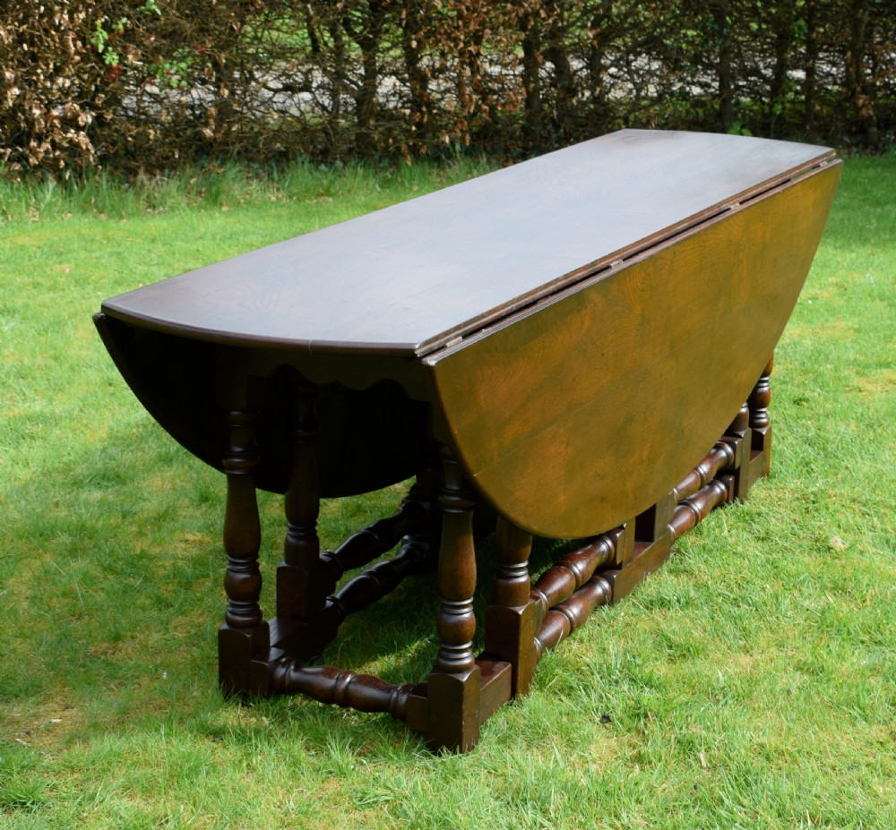 An early twentieth-century dark oak oval wake dining table with two drop-leaf flaps, turned legs, and base stretchers. View XIII