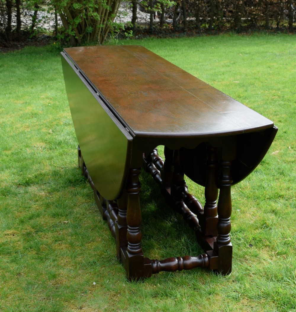 An early twentieth-century dark oak oval wake dining table with two drop-leaf flaps, turned legs, and base stretchers. View XIV