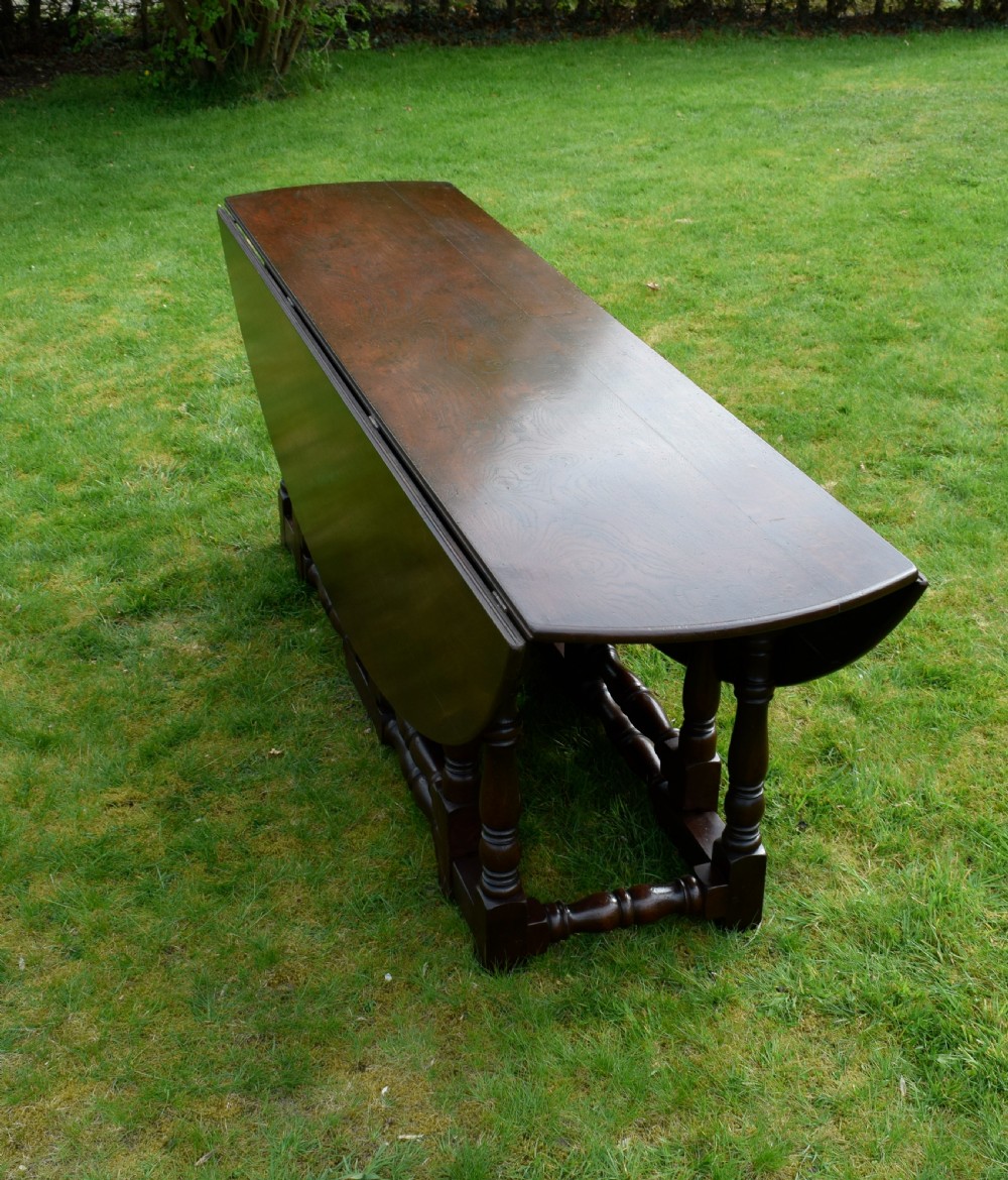 An early twentieth-century dark oak oval wake dining table with two drop-leaf flaps, turned legs, and base stretchers. View XV
