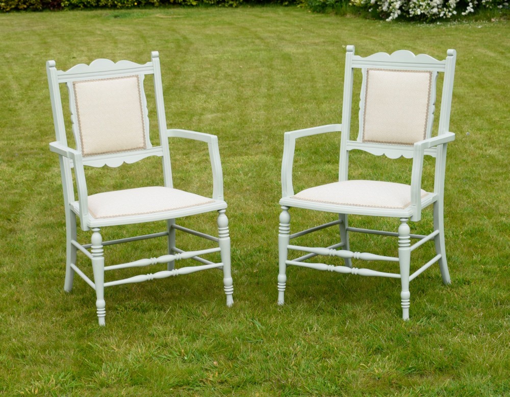 A pair of painted pale green Edwardian open armchairs featuring cream upholstered seats, padded backrest panels, turned front legs, and scalloped top rails.