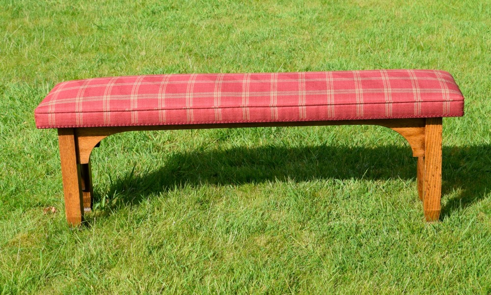 An oak window bench featuring a padded red tartan upholstered seat supported by solid oak legs with Gothic arch cut-out details. View IV