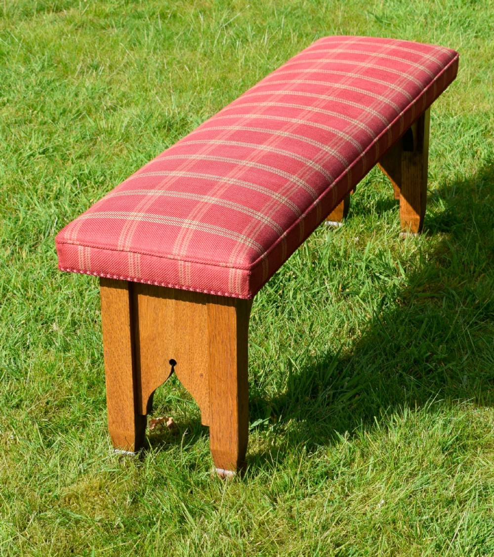 An oak window bench featuring a padded red tartan upholstered seat supported by solid oak legs with Gothic arch cut-out details. View VIII