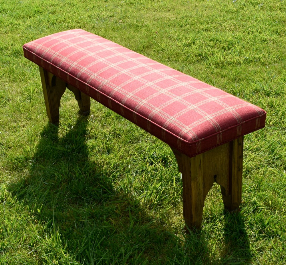An oak window bench featuring a padded red tartan upholstered seat supported by solid oak legs with Gothic arch cut-out details. View IX