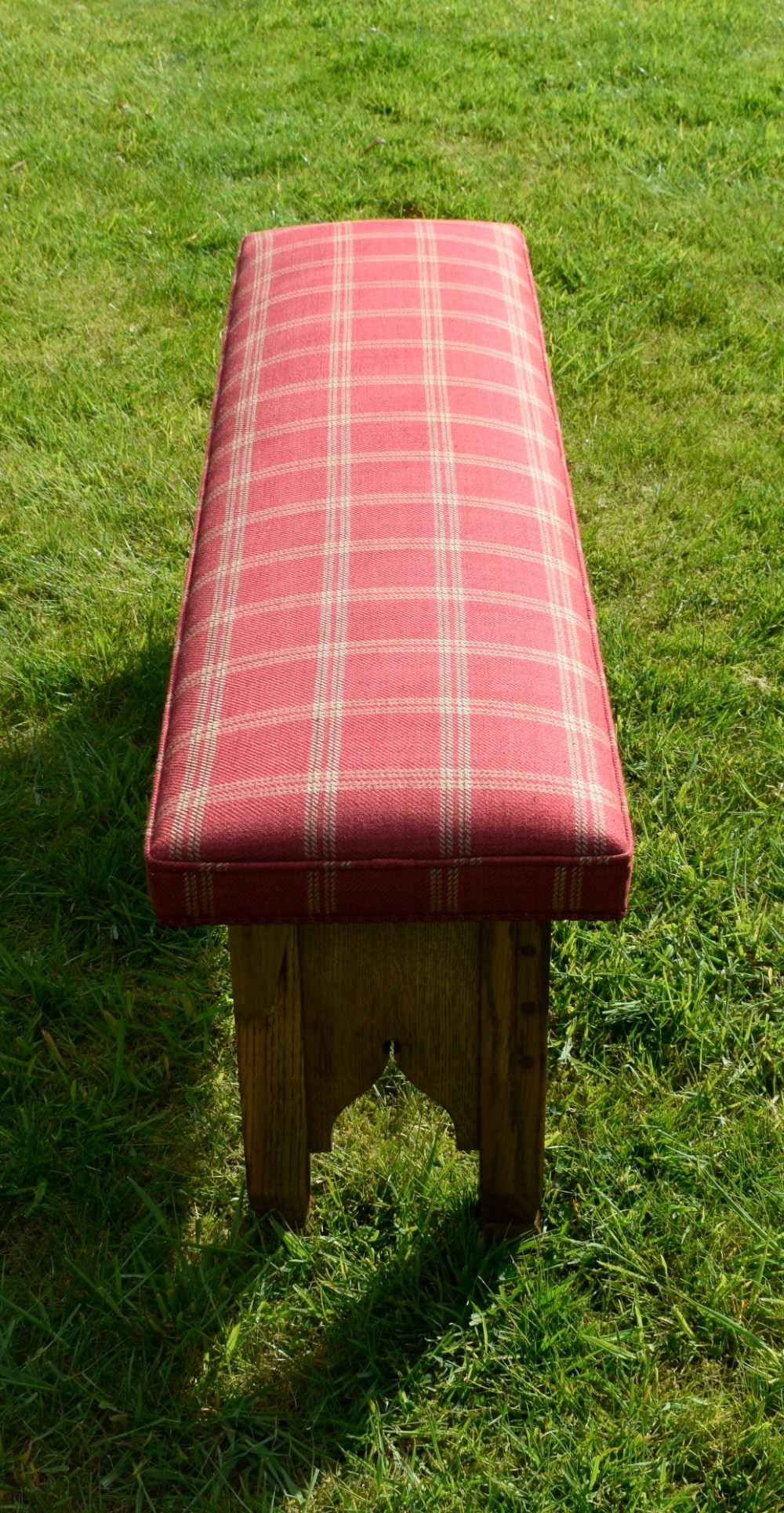 An oak window bench featuring a padded red tartan upholstered seat supported by solid oak legs with Gothic arch cut-out details. View X