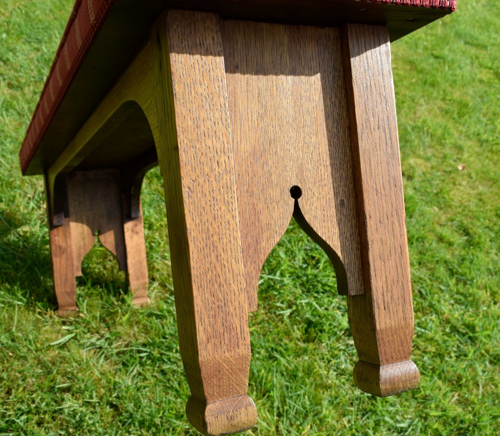 An oak window bench featuring a padded red tartan upholstered seat supported by solid oak legs with Gothic arch cut-out details. View XII