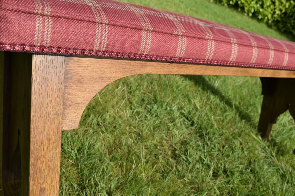 An oak window bench featuring a padded red tartan upholstered seat supported by solid oak legs with Gothic arch cut-out details. View XIV