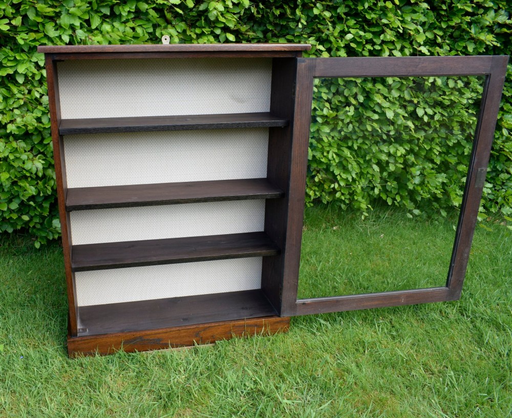 A dark oak glazed cabinet featuring a single glass door opening to internal shelving backed with a neutral patterned fabric lining. View XIII