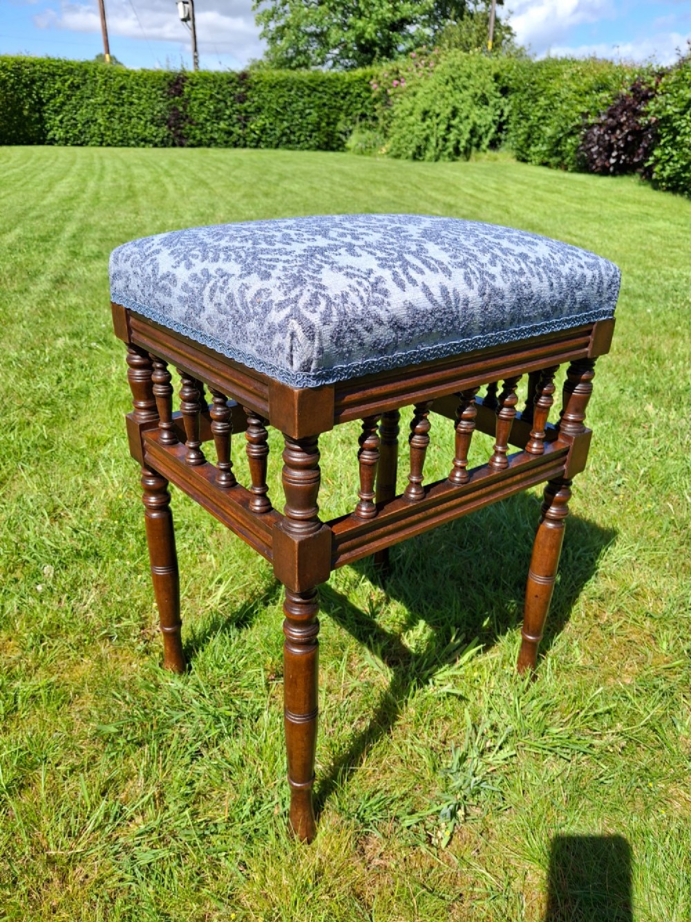 An Edwardian dark wood piano stool with turned spindles and a patterned blue fabric upholstered seat.