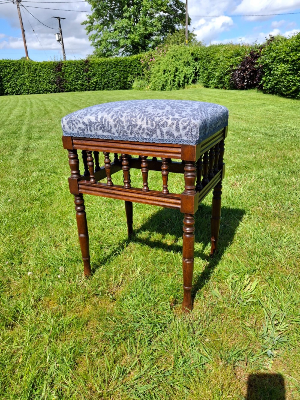 An Edwardian dark wood piano stool with turned spindles and a patterned blue fabric upholstered seat. View II