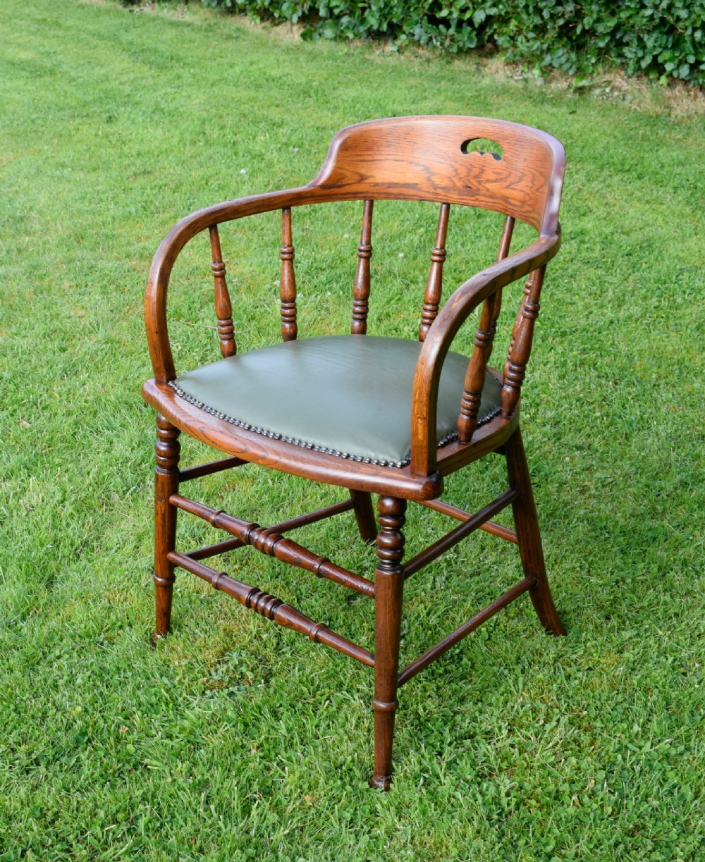An early 20th-century oak desk chair featuring turned spindles, a curved backrest with a cut-out handle, and a green leather seat fastened with brass studs. View II