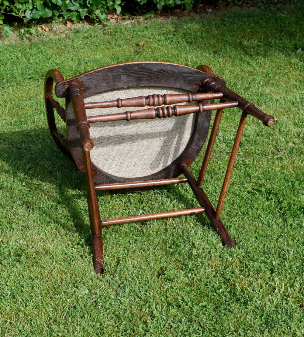 An early 20th-century oak desk chair featuring turned spindles, a curved backrest with a cut-out handle, and a green leather seat fastened with brass studs. View V