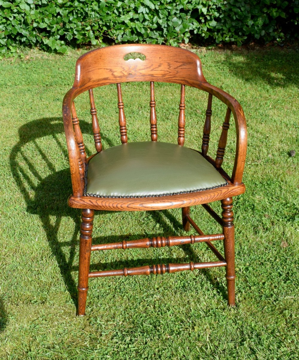 An early 20th-century oak desk chair featuring turned spindles, a curved backrest with a cut-out handle, and a green leather seat fastened with brass studs. View XIII