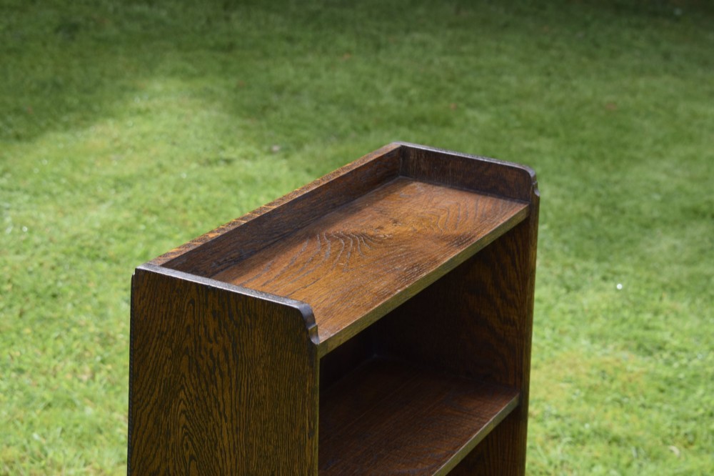 An early 20th-century open oak bookcase featuring four fixed shelves, solid side panels, and a low gallery back top. View V