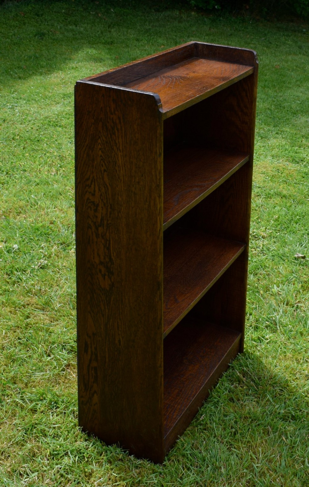 An early 20th-century open oak bookcase featuring four fixed shelves, solid side panels, and a low gallery back top. View VI