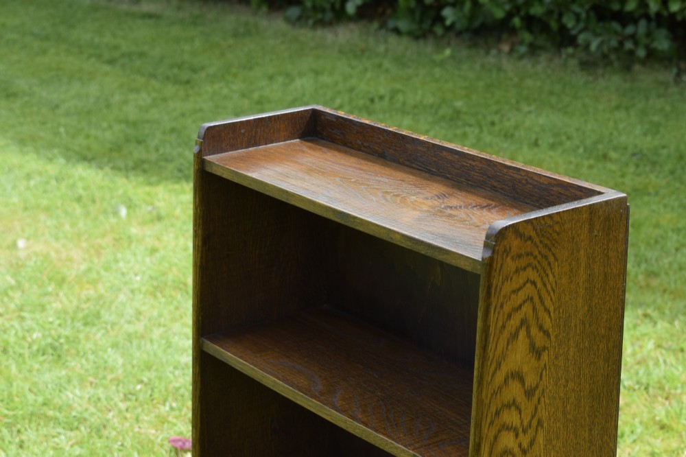 An early 20th-century open oak bookcase featuring four fixed shelves, solid side panels, and a low gallery back top. View X