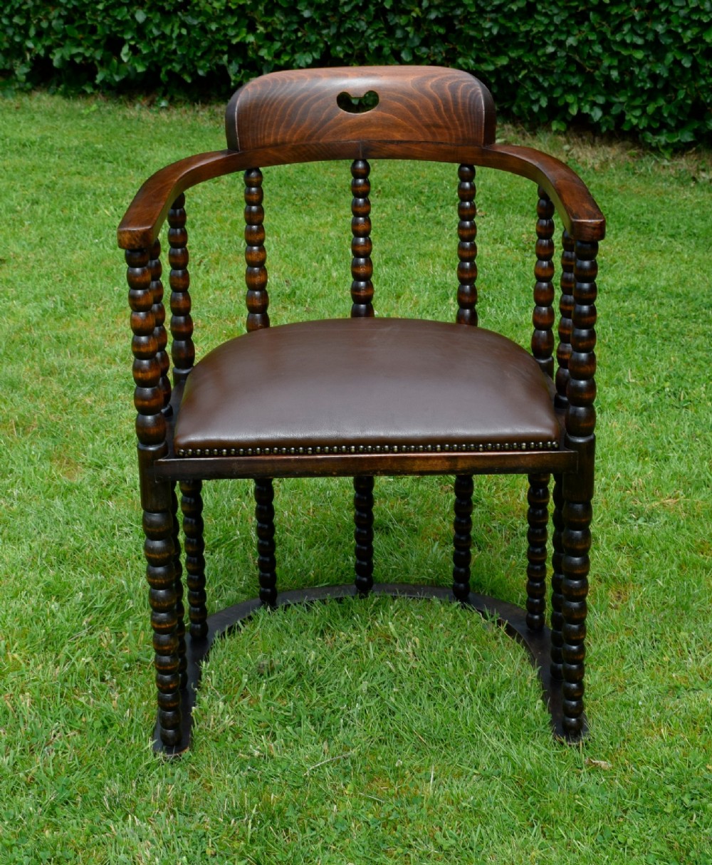 A dark oak Arts and Crafts desk chair featuring bobbin-turned uprights, a curved crest rail with a cut-out handle, and a brown leather seat fastened with brass studs. View II