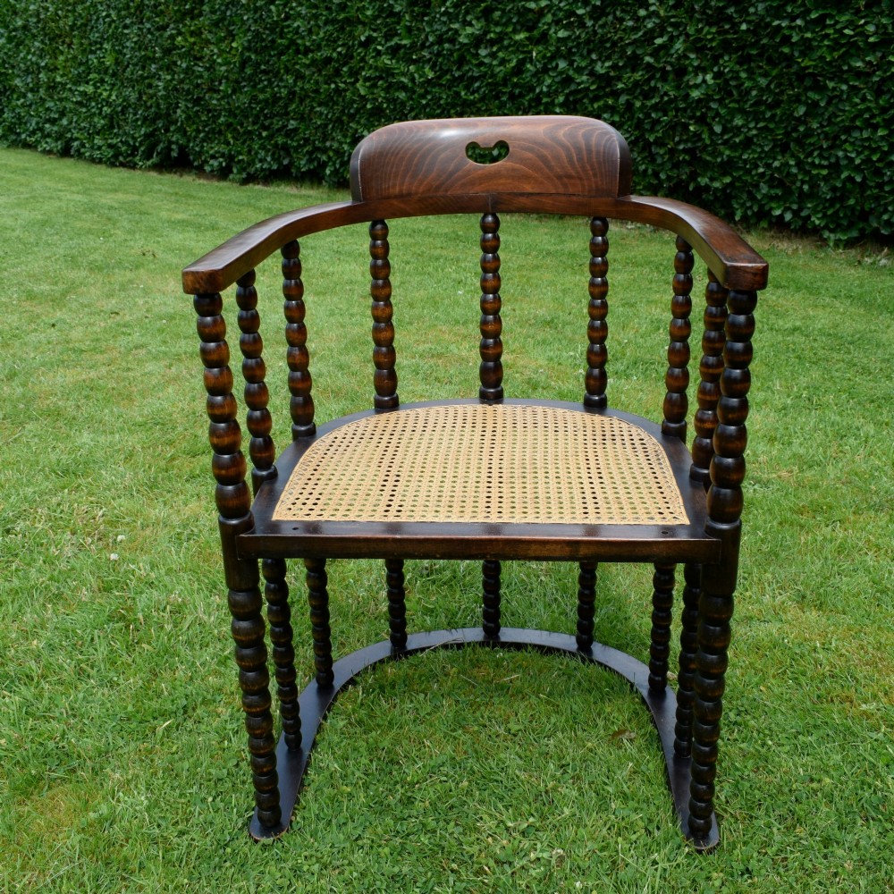 A dark oak Arts and Crafts desk chair featuring bobbin-turned uprights, a curved crest rail with a cut-out handle, and a brown leather seat fastened with brass studs. View III