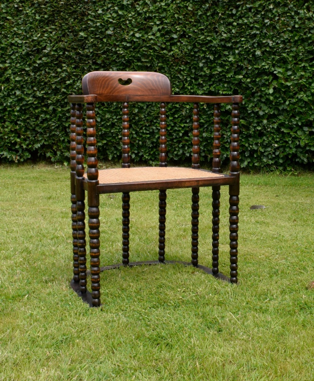 A dark oak Arts and Crafts desk chair featuring bobbin-turned uprights, a curved crest rail with a cut-out handle, and a brown leather seat fastened with brass studs. View IV