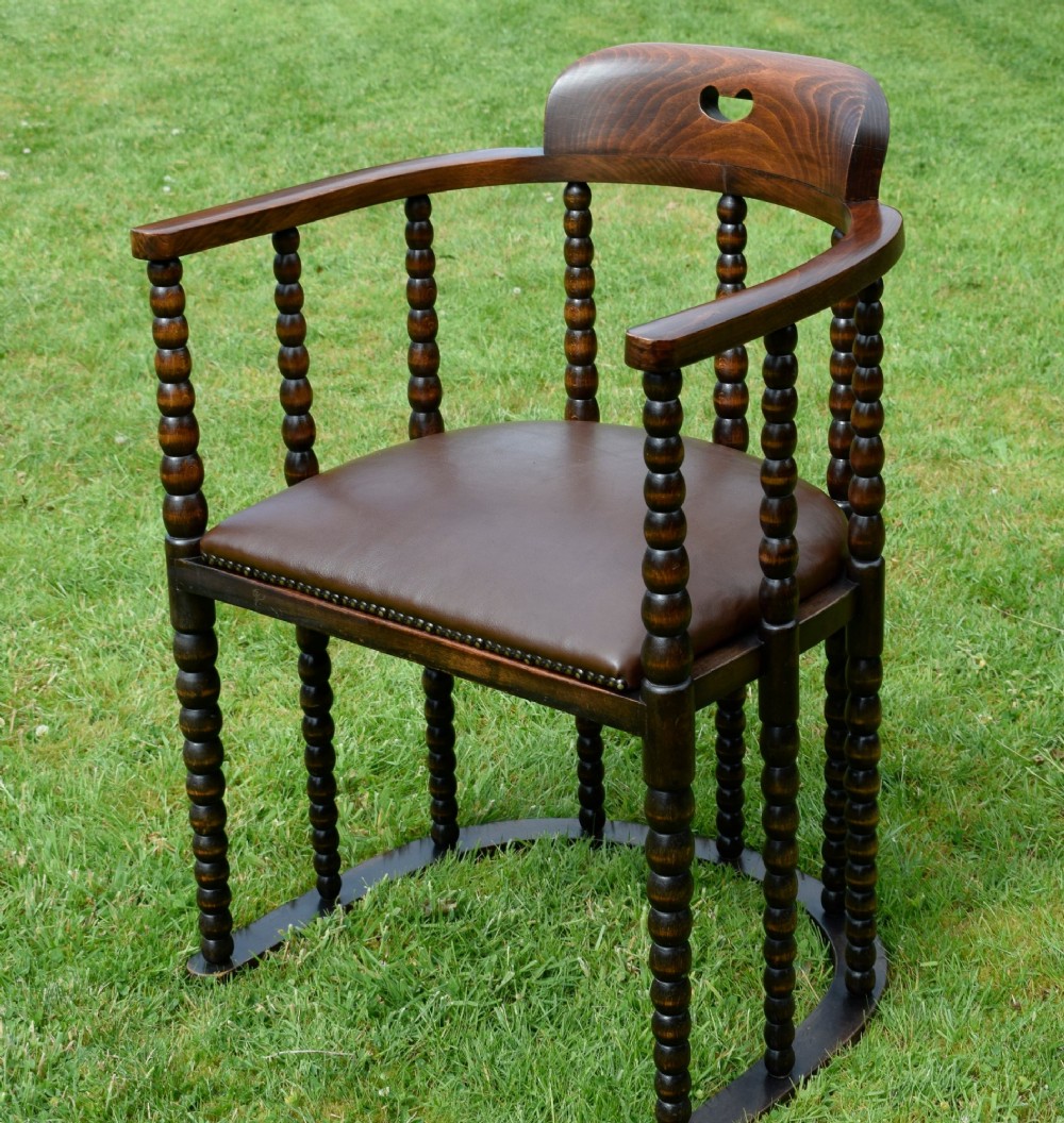 A dark oak Arts and Crafts desk chair featuring bobbin-turned uprights, a curved crest rail with a cut-out handle, and a brown leather seat fastened with brass studs. View VIII