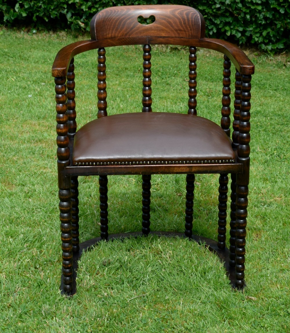 A dark oak Arts and Crafts desk chair featuring bobbin-turned uprights, a curved crest rail with a cut-out handle, and a brown leather seat fastened with brass studs. View IX