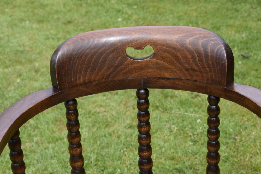 A dark oak Arts and Crafts desk chair featuring bobbin-turned uprights, a curved crest rail with a cut-out handle, and a brown leather seat fastened with brass studs. View XI