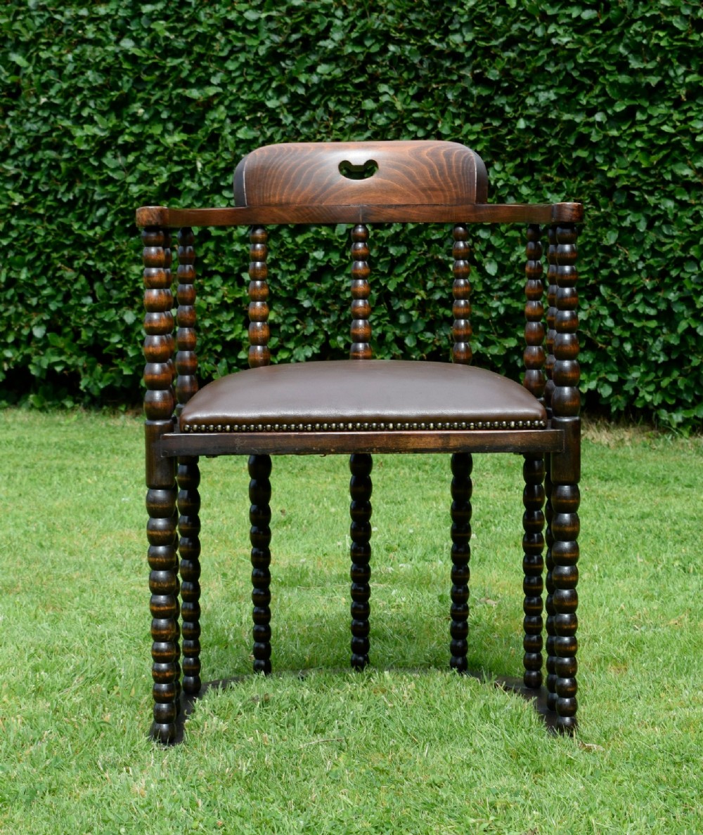 A dark oak Arts and Crafts desk chair featuring bobbin-turned uprights, a curved crest rail with a cut-out handle, and a brown leather seat fastened with brass studs. View XIII