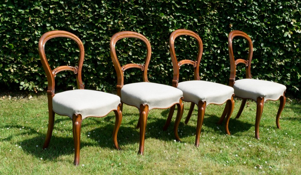A set of four Victorian walnut balloon-back dining chairs with carved mid-rails, neutral upholstered seats, and cabriole front legs. View II