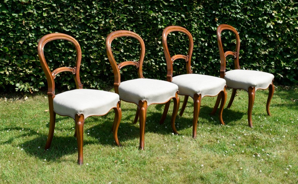 A set of four Victorian walnut balloon-back dining chairs with carved mid-rails, neutral upholstered seats, and cabriole front legs. View III