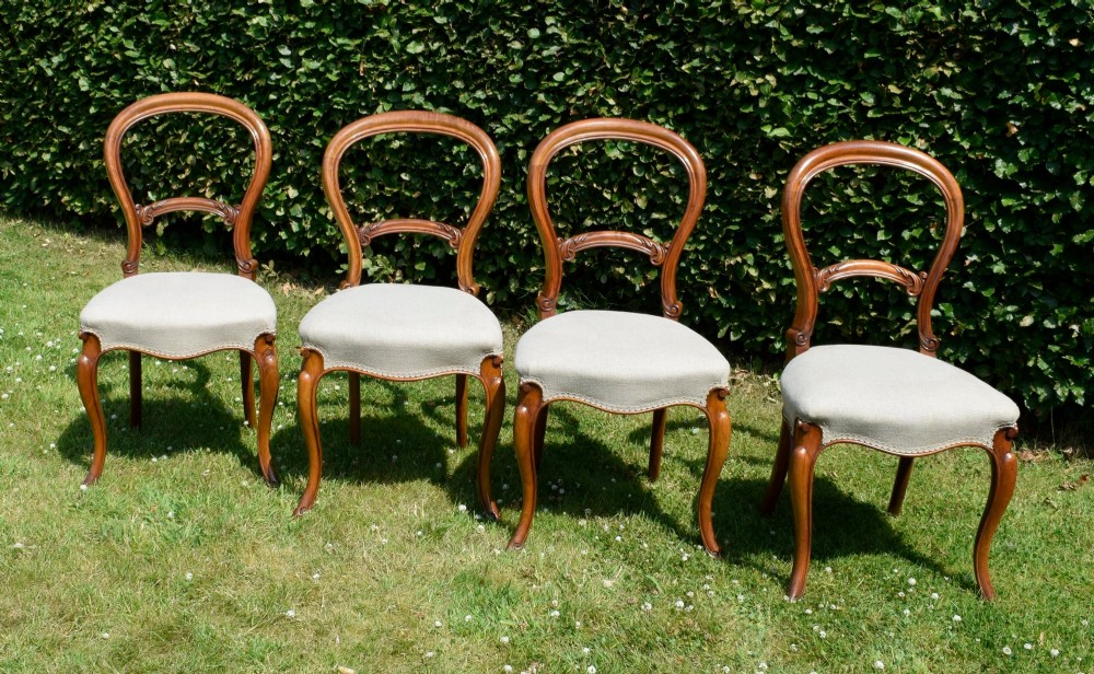 A set of four Victorian walnut balloon-back dining chairs with carved mid-rails, neutral upholstered seats, and cabriole front legs. View IV