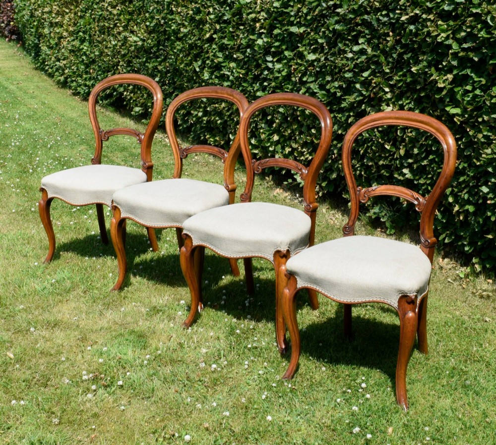 A set of four Victorian walnut balloon-back dining chairs with carved mid-rails, neutral upholstered seats, and cabriole front legs. View V