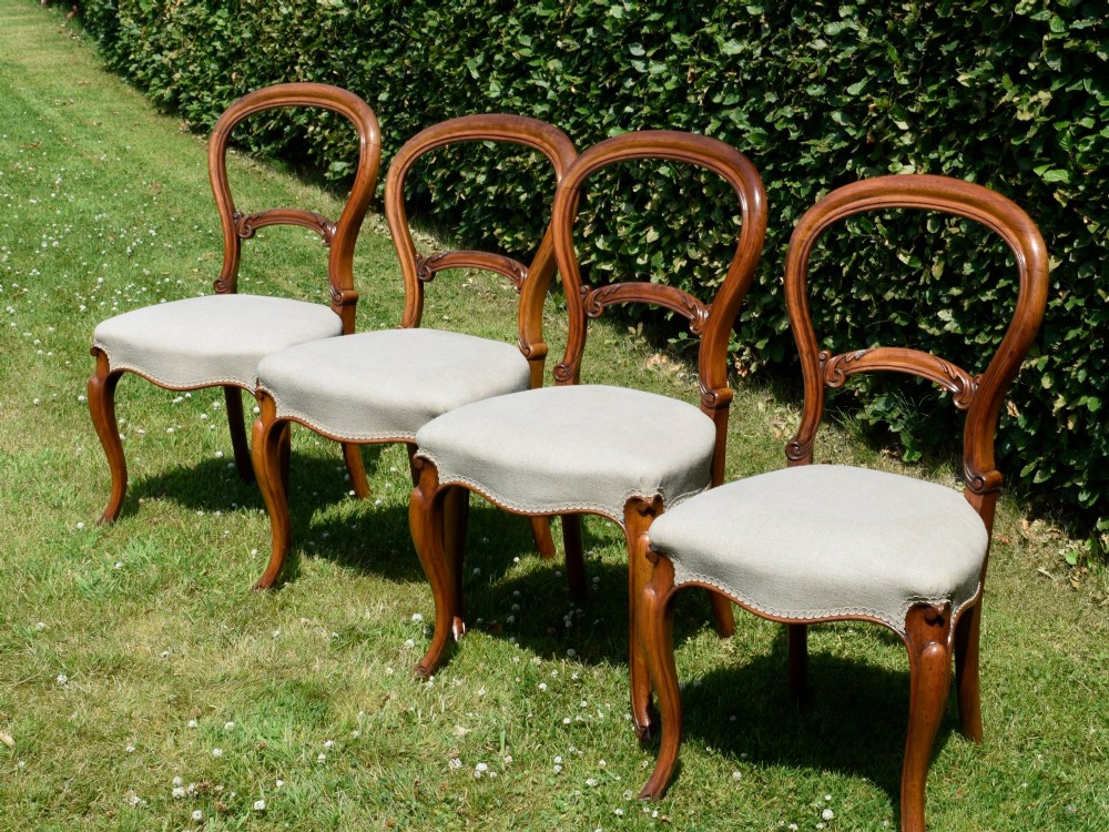 A set of four Victorian walnut balloon-back dining chairs with carved mid-rails, neutral upholstered seats, and cabriole front legs. View VI
