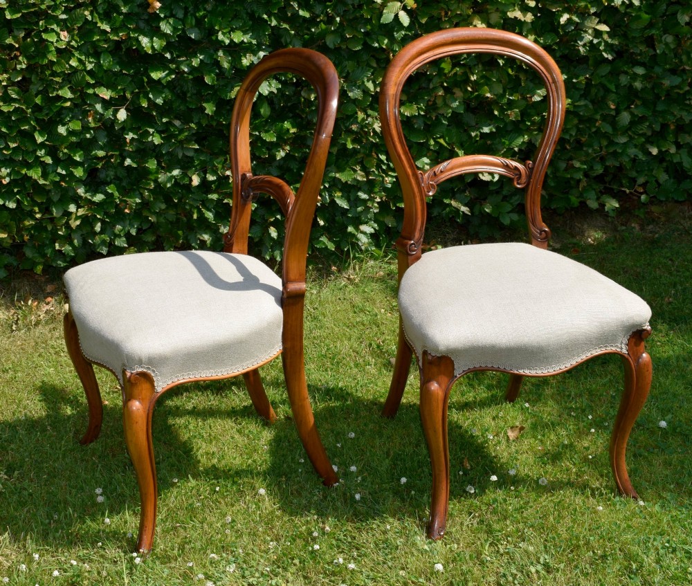 A set of four Victorian walnut balloon-back dining chairs with carved mid-rails, neutral upholstered seats, and cabriole front legs. View VII