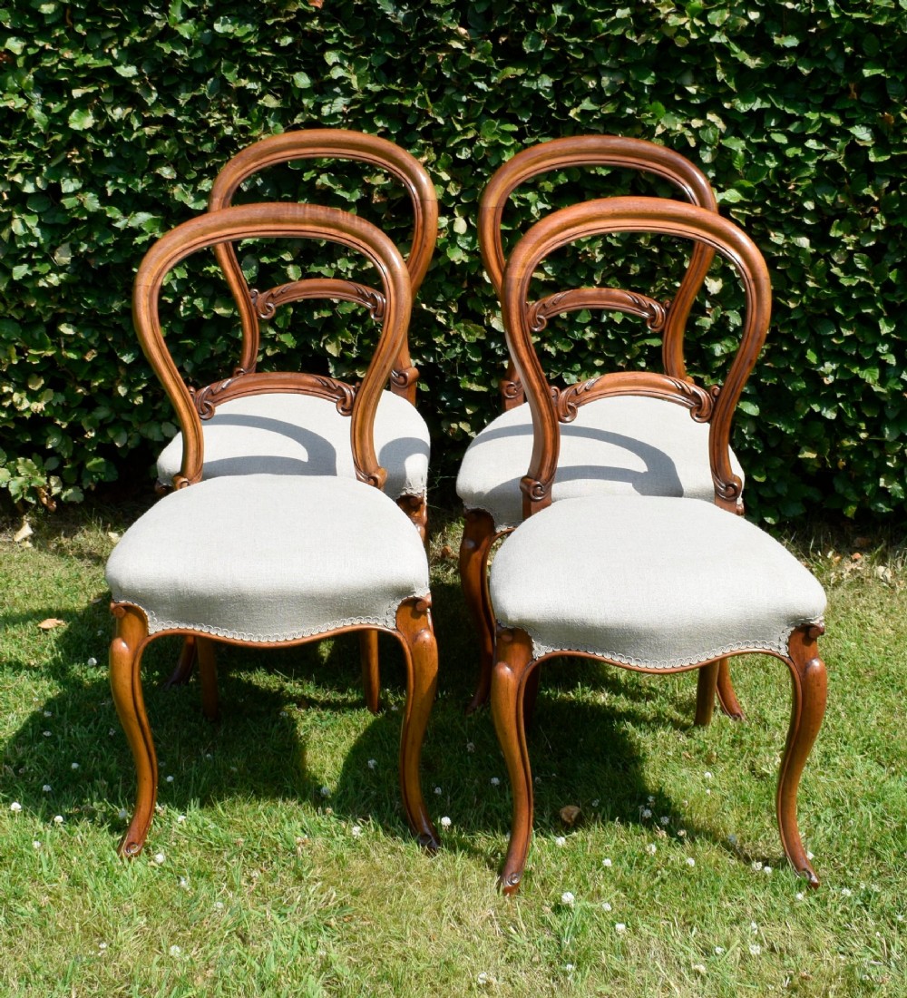 A set of four Victorian walnut balloon-back dining chairs with carved mid-rails, neutral upholstered seats, and cabriole front legs. View VIII