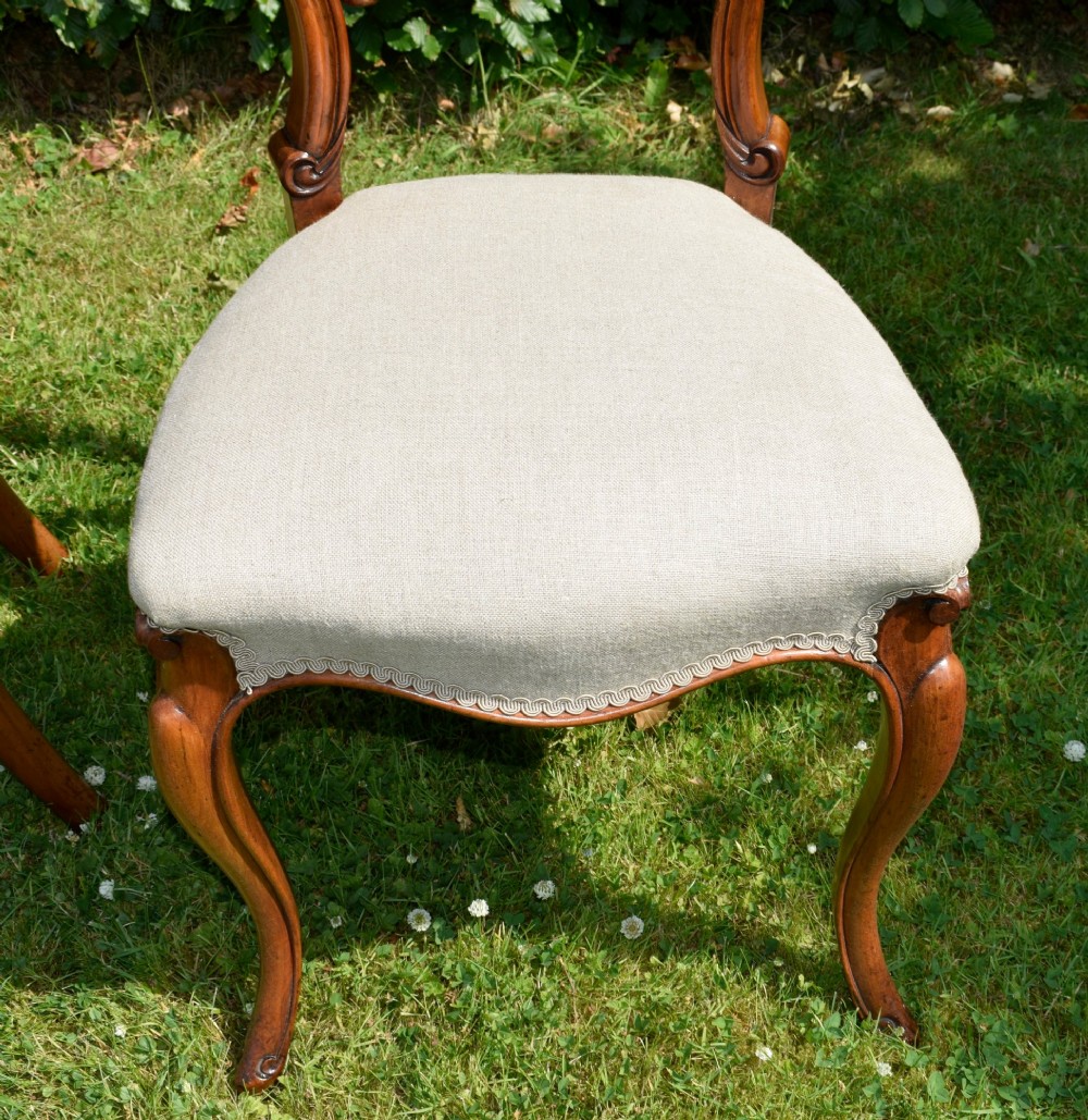 A set of four Victorian walnut balloon-back dining chairs with carved mid-rails, neutral upholstered seats, and cabriole front legs. View X