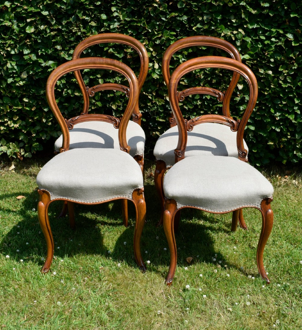 A set of four Victorian walnut balloon-back dining chairs with carved mid-rails, neutral upholstered seats, and cabriole front legs. View XIV