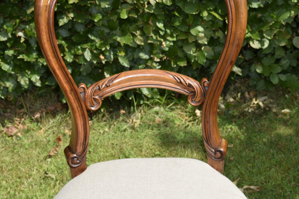 A set of four Victorian walnut balloon-back dining chairs with carved mid-rails, neutral upholstered seats, and cabriole front legs. View XV