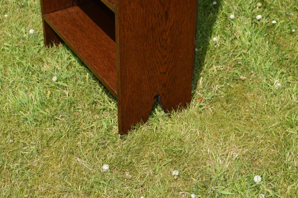 A slim, open-front Arts and Crafts oak bookcase with five shelves, cut-out side panels, and a low galleried top featuring a subtle central carved motif. View IV