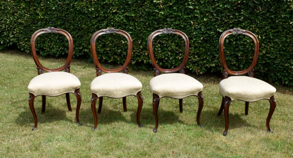 A set of four Victorian walnut dining chairs featuring carved balloon backs, cream upholstered seats, and curved cabriole legs.
