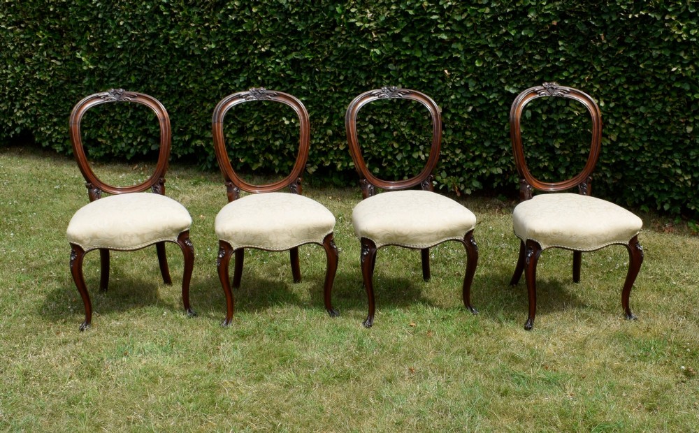 A set of four Victorian walnut dining chairs featuring carved balloon backs, cream upholstered seats, and curved cabriole legs. View II