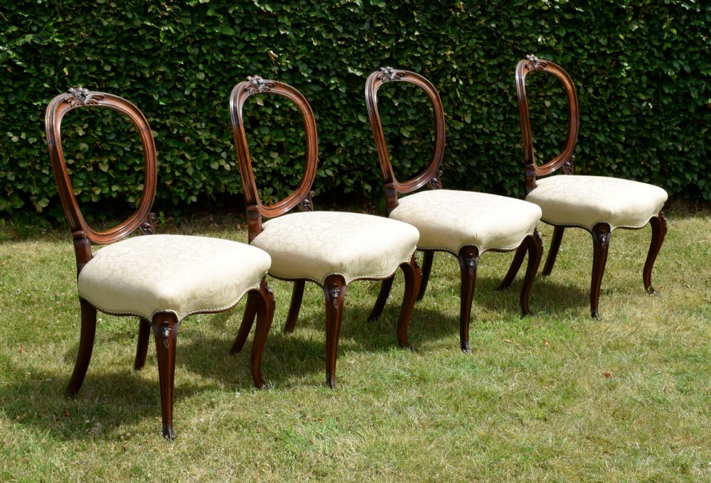 A set of four Victorian walnut dining chairs featuring carved balloon backs, cream upholstered seats, and curved cabriole legs. View IV