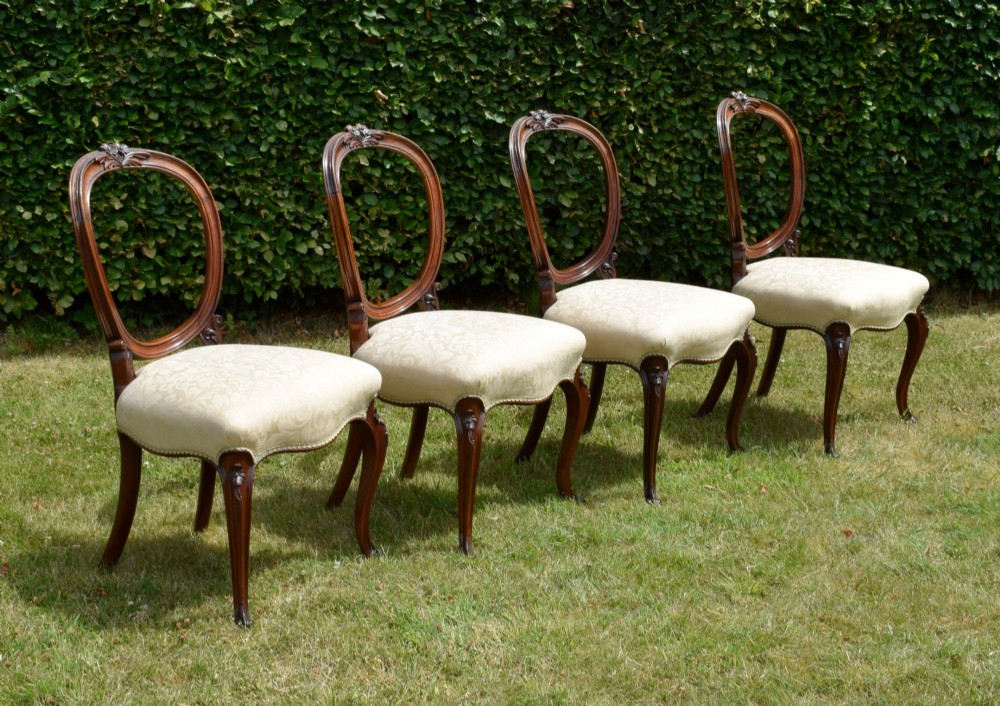 A set of four Victorian walnut dining chairs featuring carved balloon backs, cream upholstered seats, and curved cabriole legs. View V