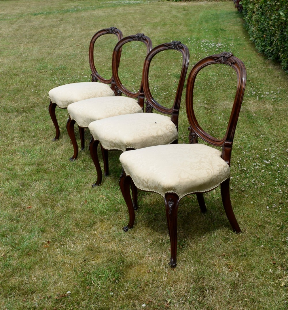 A set of four Victorian walnut dining chairs featuring carved balloon backs, cream upholstered seats, and curved cabriole legs. View VI