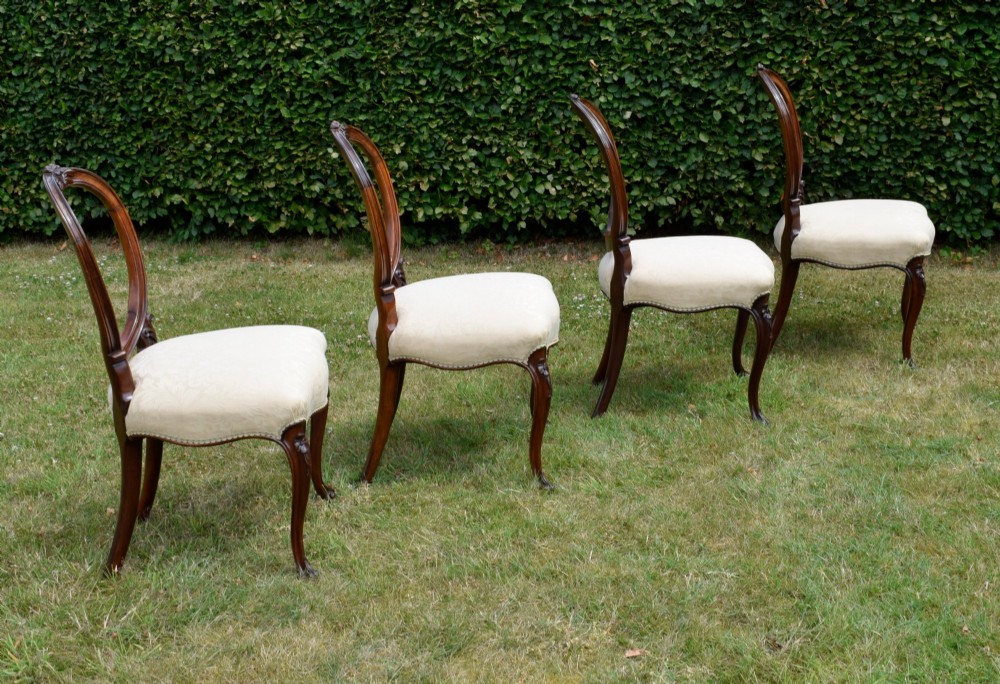 A set of four Victorian walnut dining chairs featuring carved balloon backs, cream upholstered seats, and curved cabriole legs. View VII