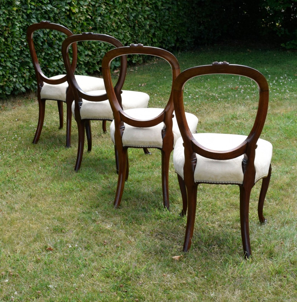 A set of four Victorian walnut dining chairs featuring carved balloon backs, cream upholstered seats, and curved cabriole legs. View VIII