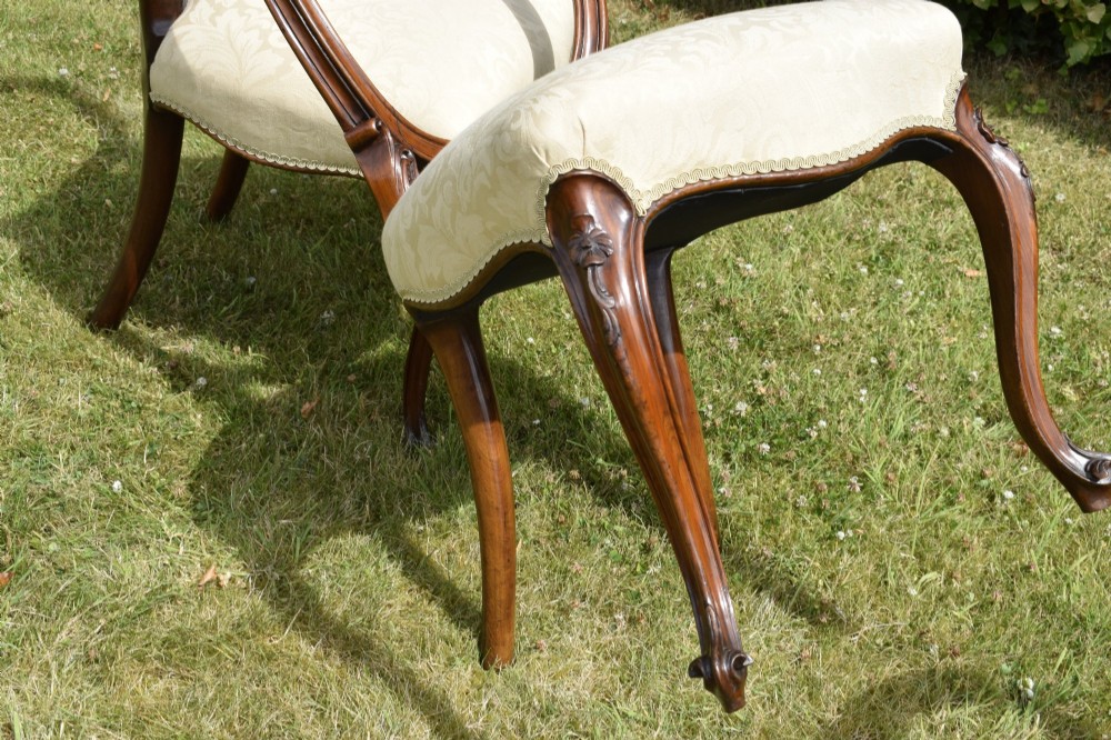 A set of four Victorian walnut dining chairs featuring carved balloon backs, cream upholstered seats, and curved cabriole legs. View X